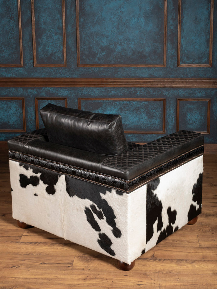 Black and white cowhide chair with leather top against a blue paneled wall.