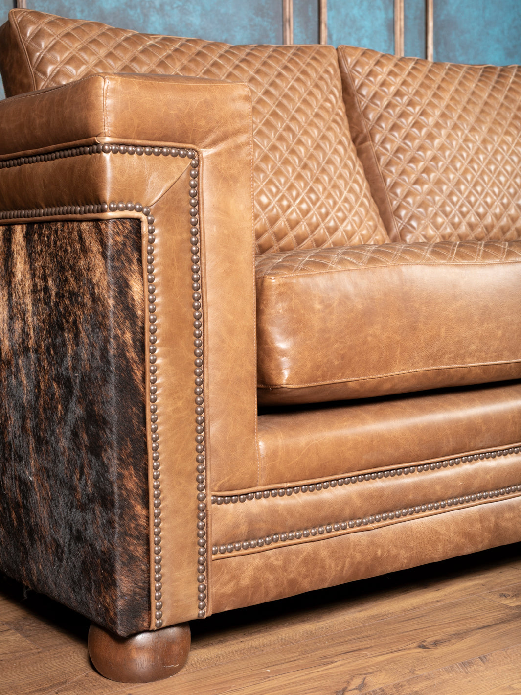 Detail of side arm on Western leather sofa showing full grain tan leather, cowhide panels and decorative nailheads