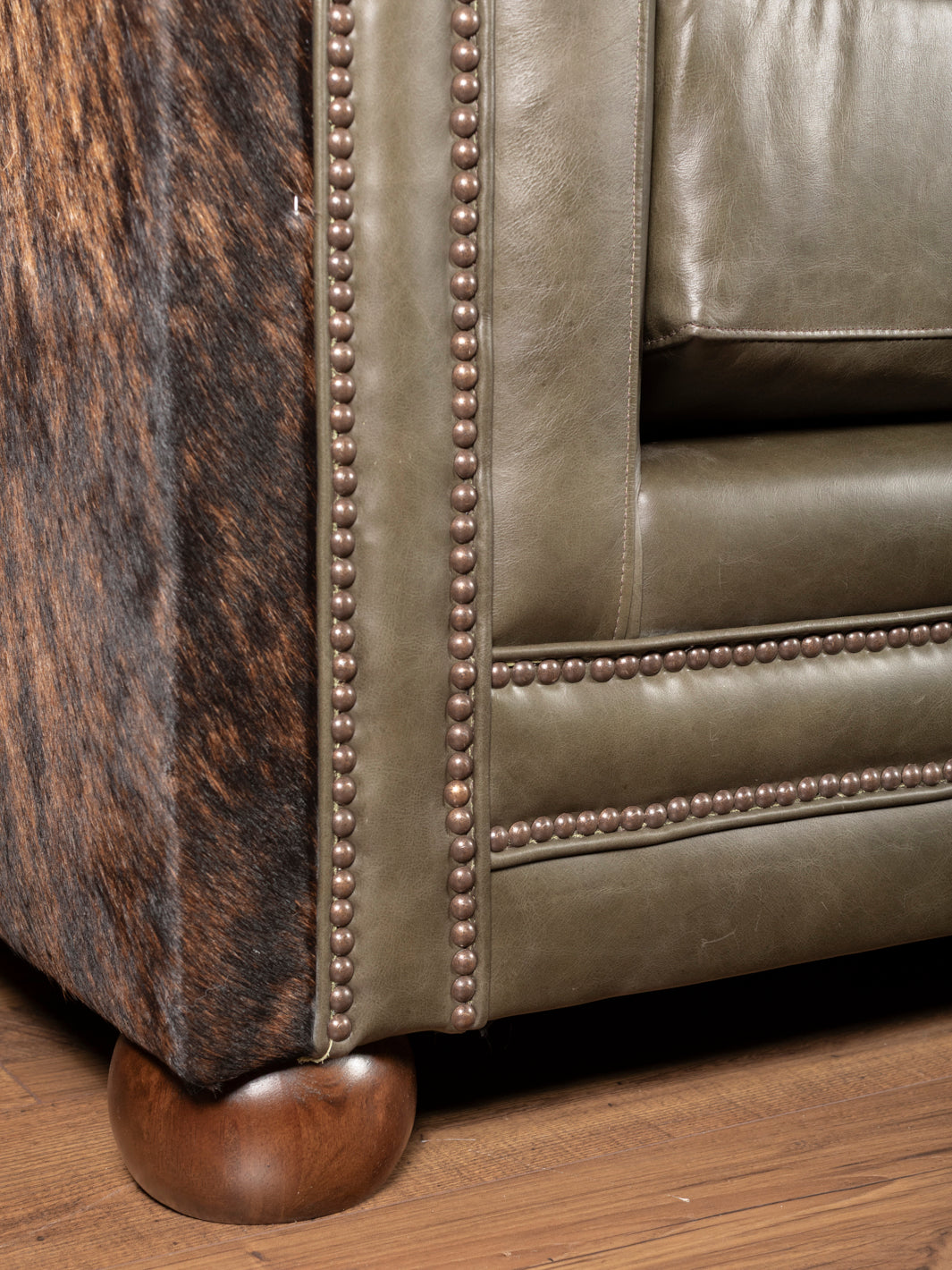 Close-up of a leather sofa with nailhead trim and wooden feet.