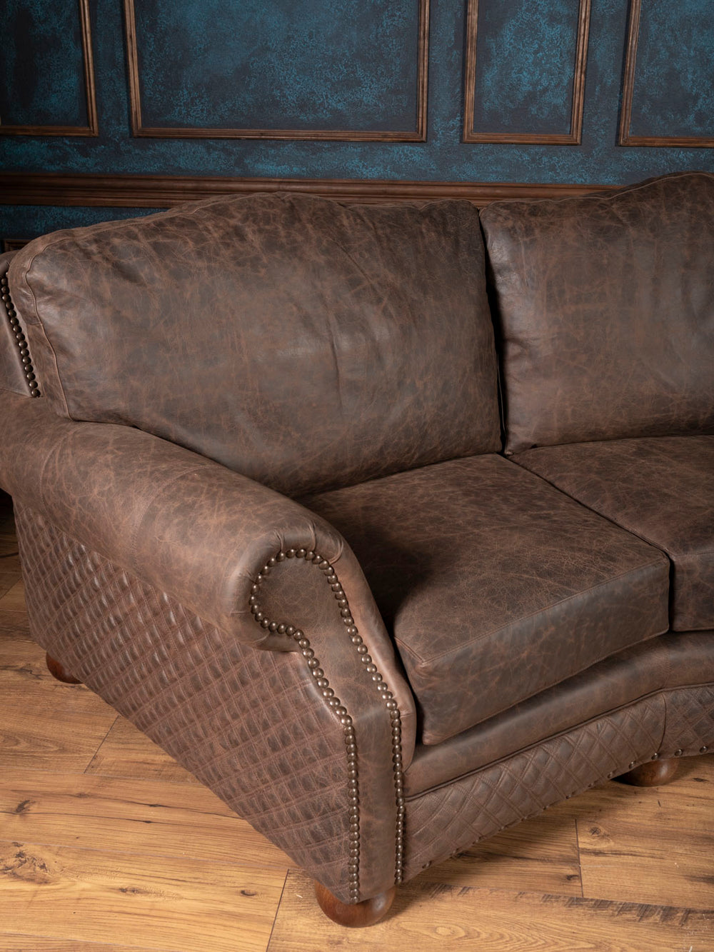 Side angle of brown leather sofa showcasing rolled arm design and quilted leather accents