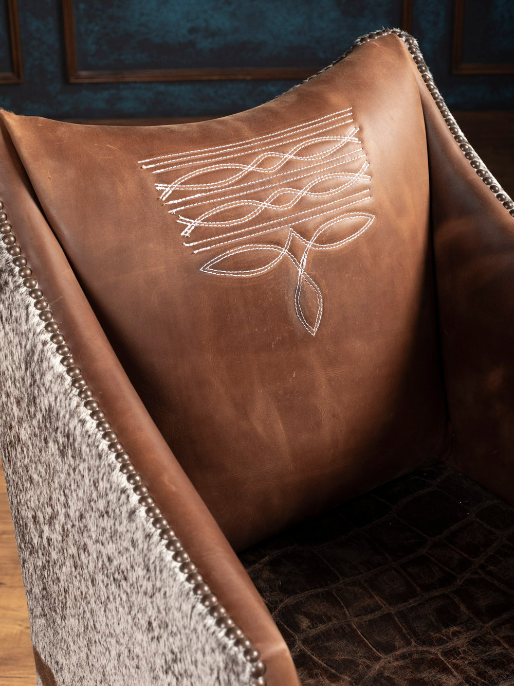 Side profile of the boot stitched leather arm chair with rich brown leather, sloped arms, and cowhide panel detailing