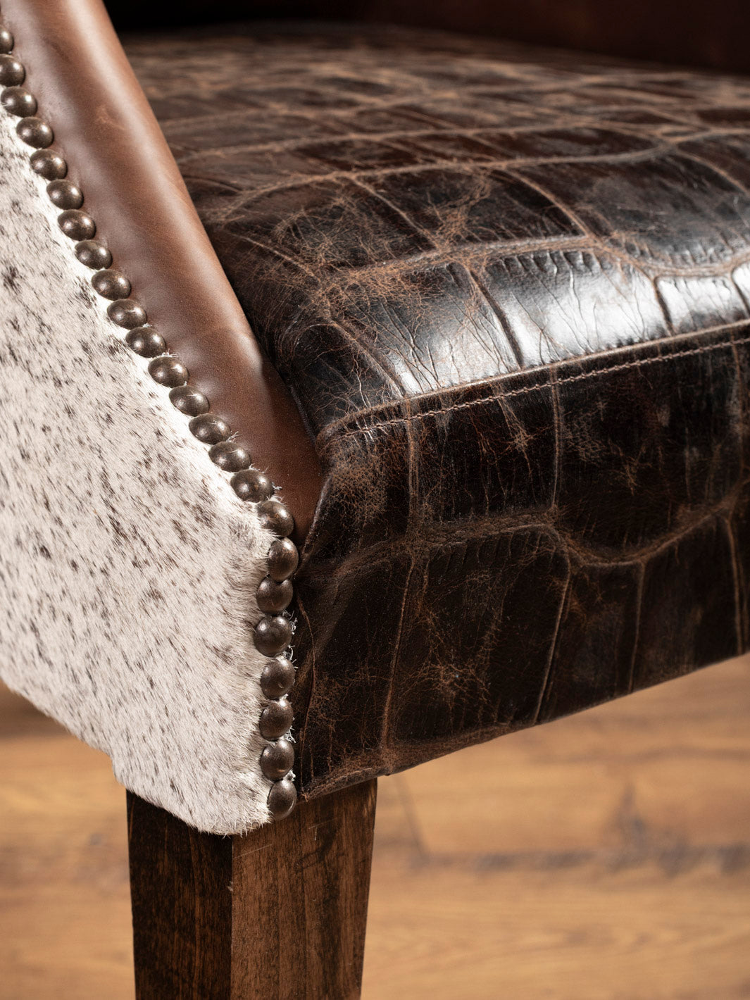 Close-up of a brown leather chair with decorative nailhead trim on a wooden floor.