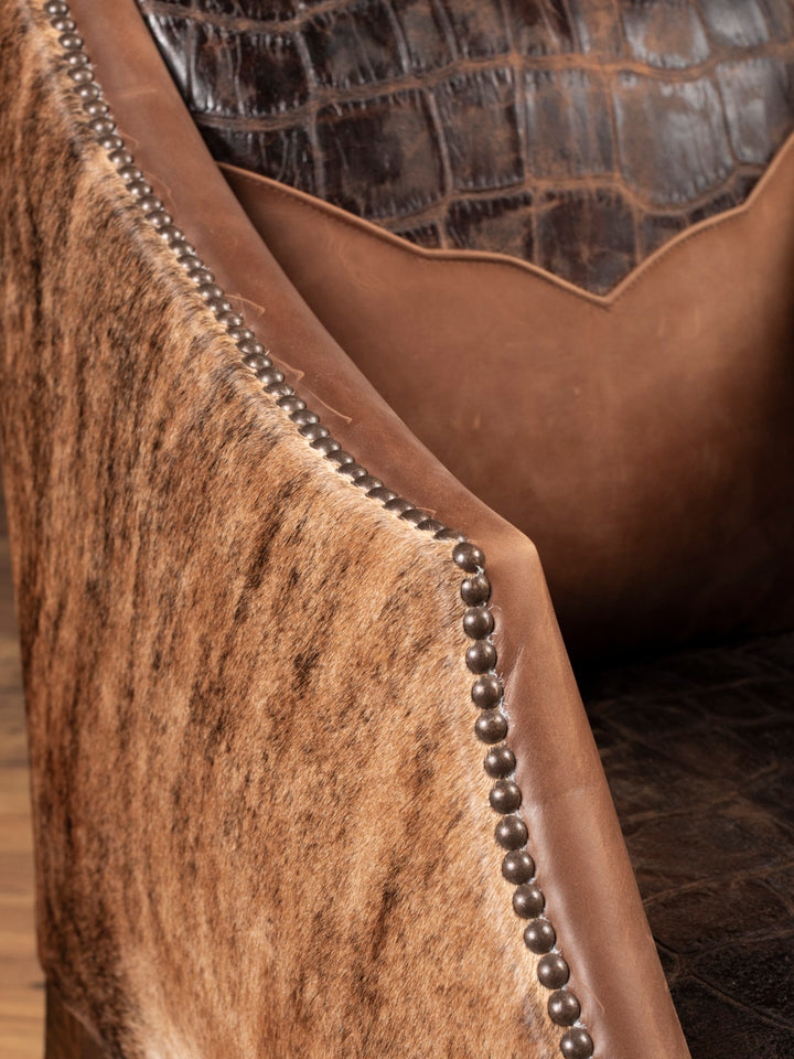 Close-up of a brown leather chair with decorative stitching, nailheads, and detailed accents.