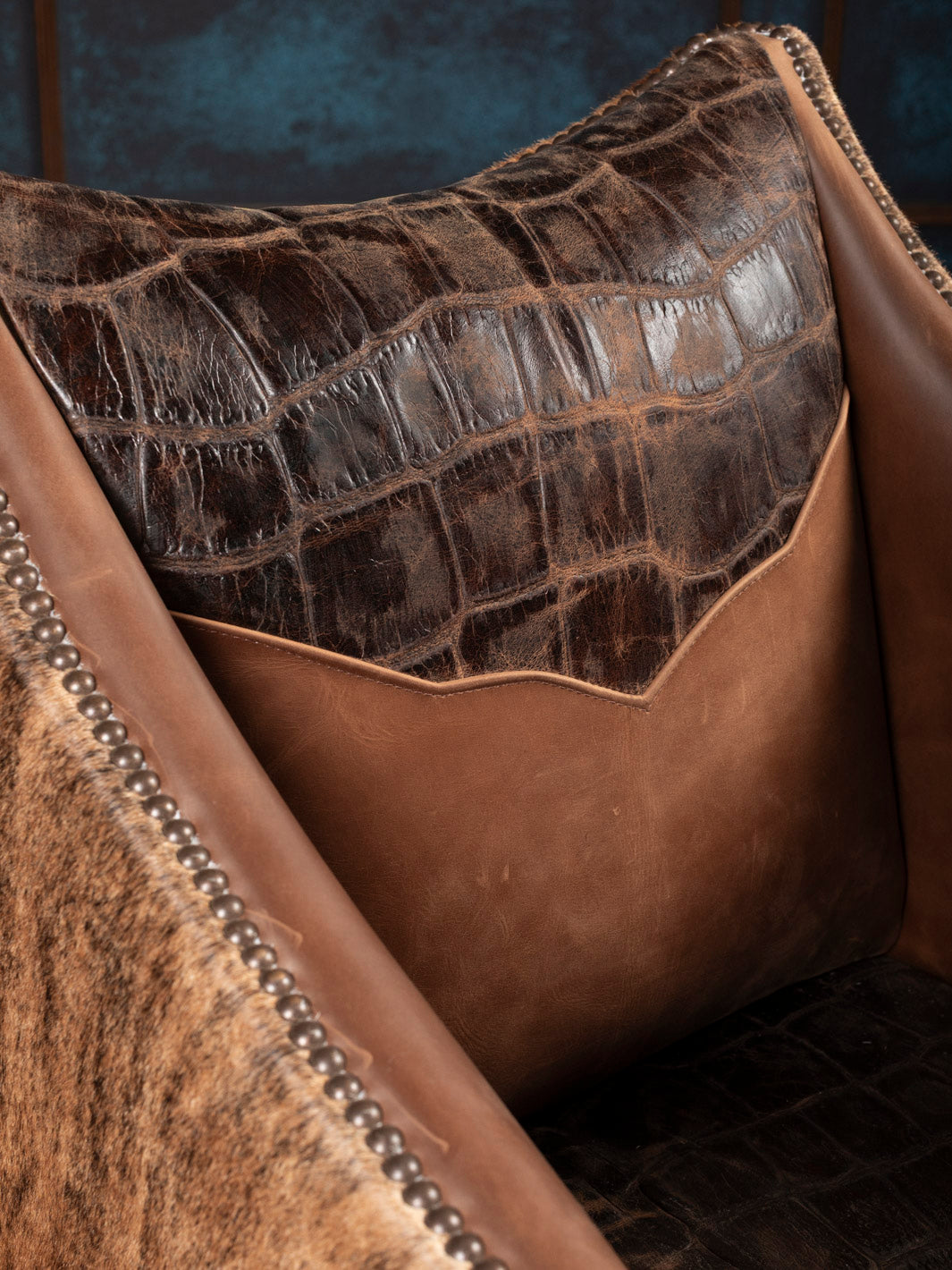 Close-up of a brown leather back cushion with gator texture and studded details.
