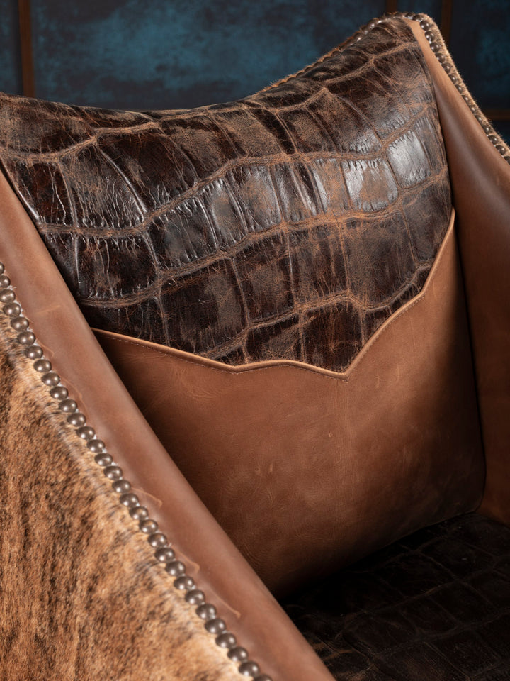 Close-up of a brown leather back cushion with gator texture and studded details.