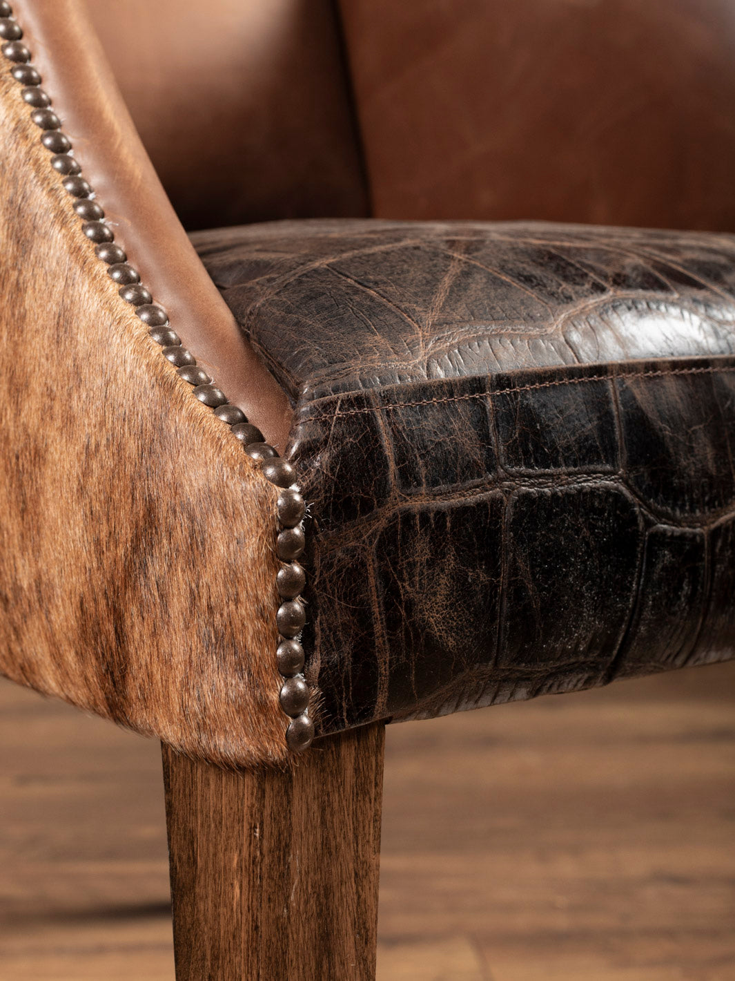 Close-up of a brown leather chair with gator seat and wooden legs.