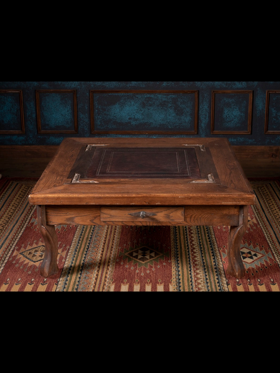 Wooden desk with leather surface in a room with patterned rug and decorative wall.