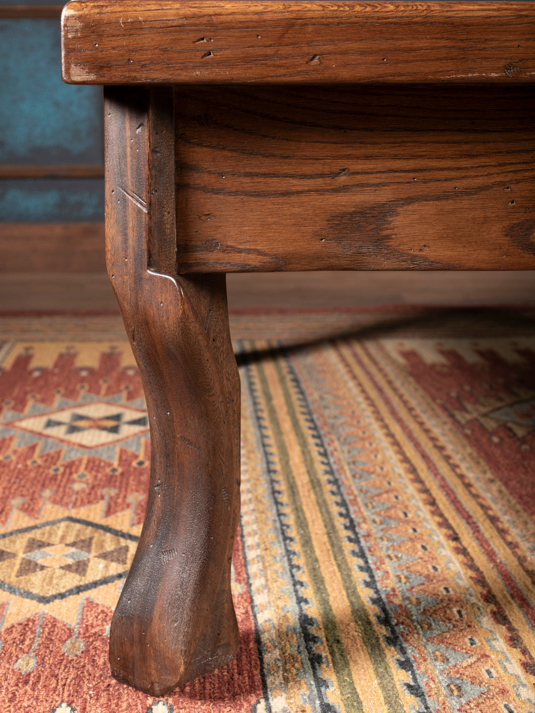 Close-up of a wooden leg on a piece of furniture with a patterned rug in the background