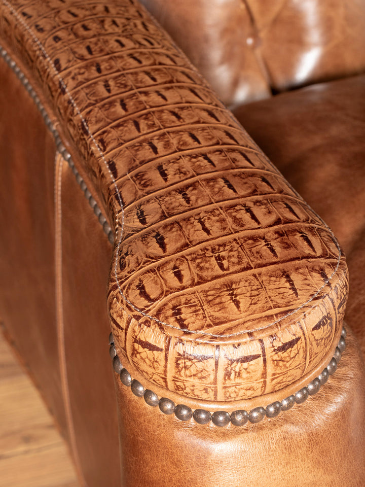 Close-up of a brown leather armrest with crocodile texture and nailhead detailing.