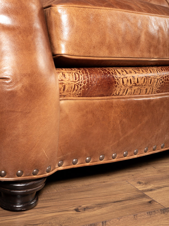 Close-up of a brown leather sofa with embossed pattern and nailhead trim on a wooden floor.