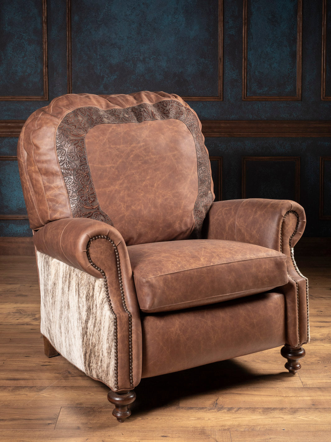 Brown leather recliner chair with patterned armrests in a room with wooden flooring and dark paneled walls.