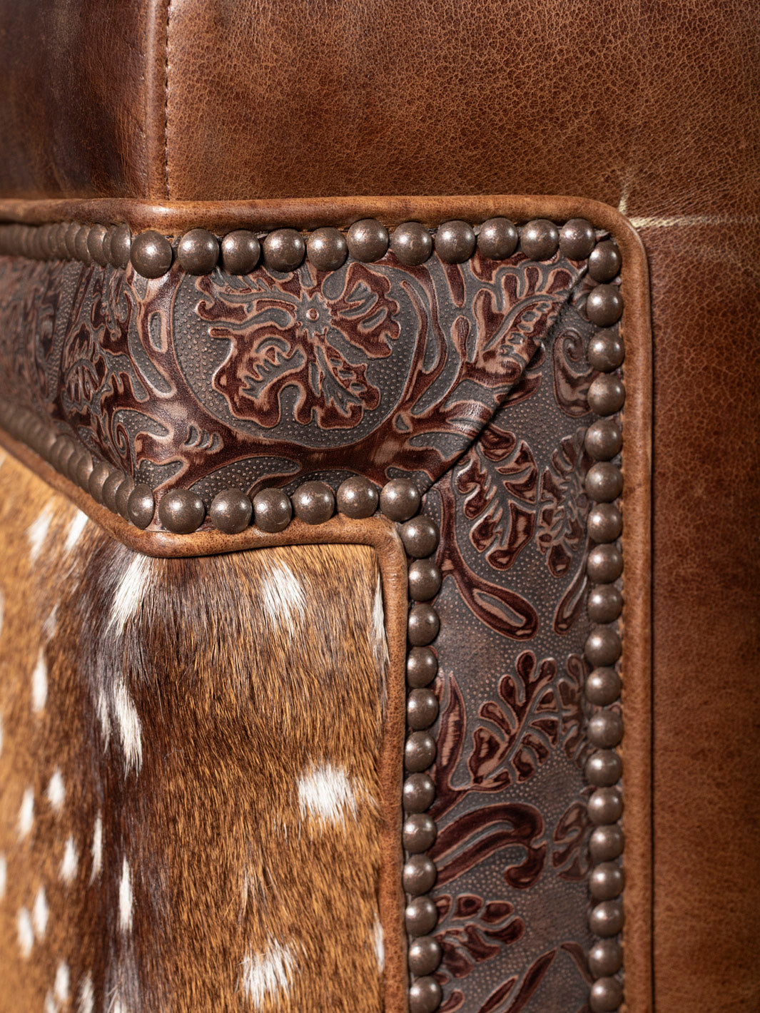 Close-up of a leather product with intricate floral embossing and metal studs.