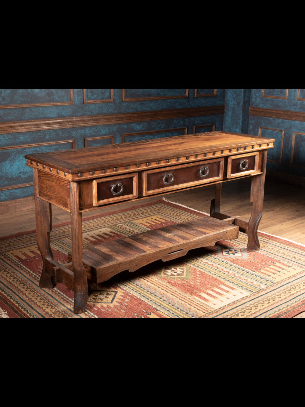 Wooden console table with drawers in a room with patterned wallpaper and rug.