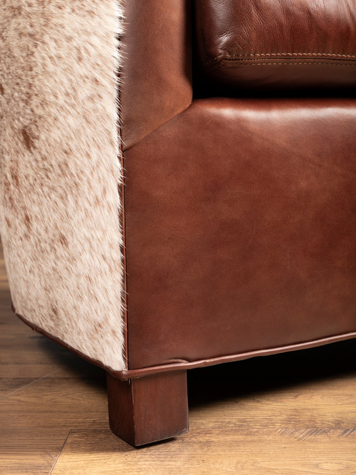 Lower corner of Western leather accent chair showing speckled cowhide, cushion and wood leg"