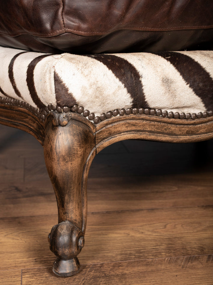 Artisan-carved wood leg and zebra hide upholstery detail on luxury animal hide ottoman
