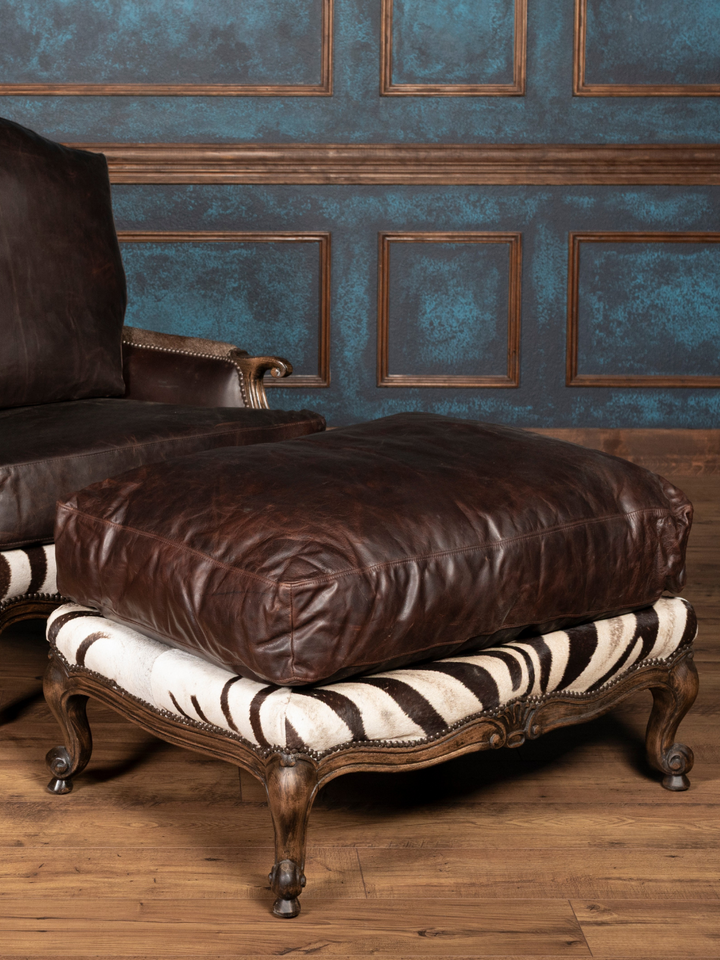 Brown leather ottoman with zebra print base trim and matching chair in background
