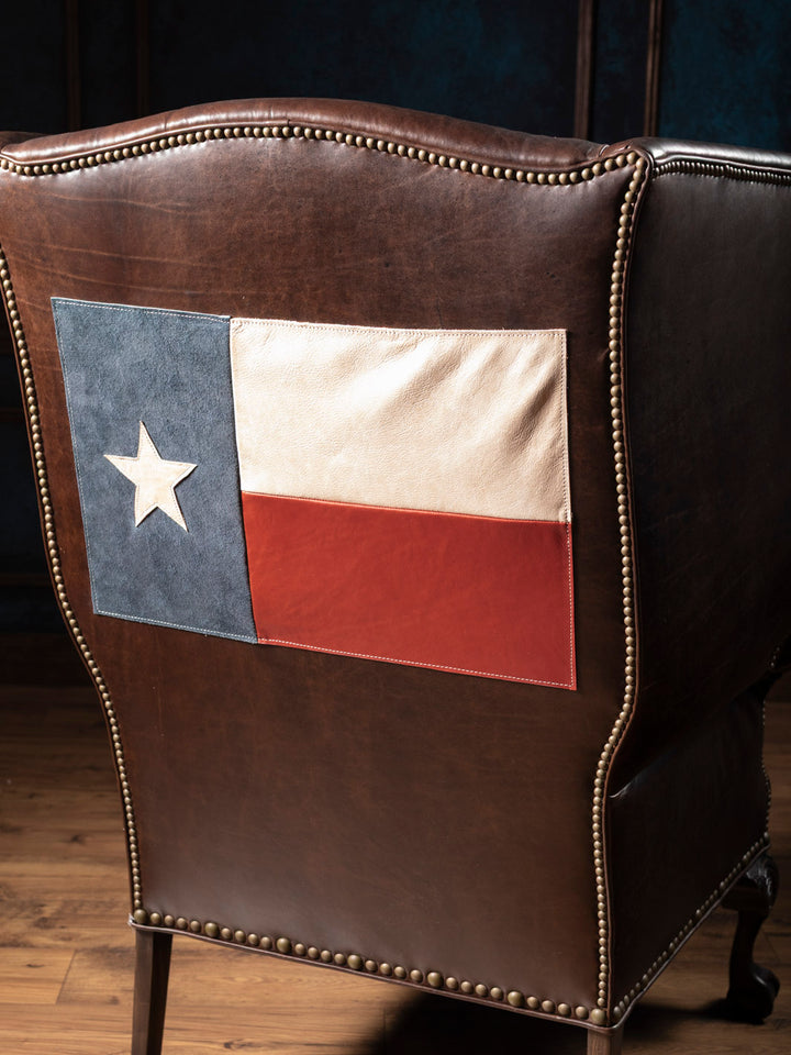 Brown leather chair with a Texas flag patch on a dark background