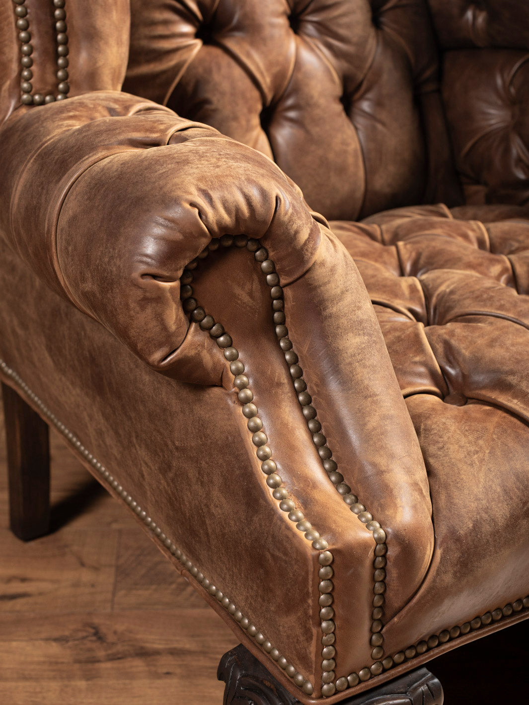 Angled view showing tufted backrest and rolled arms on handcrafted leather wingback chair