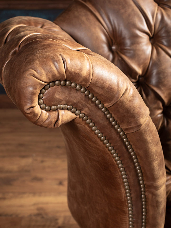 Close-up of a brown leather armchair with tufted backrest and wooden floor.