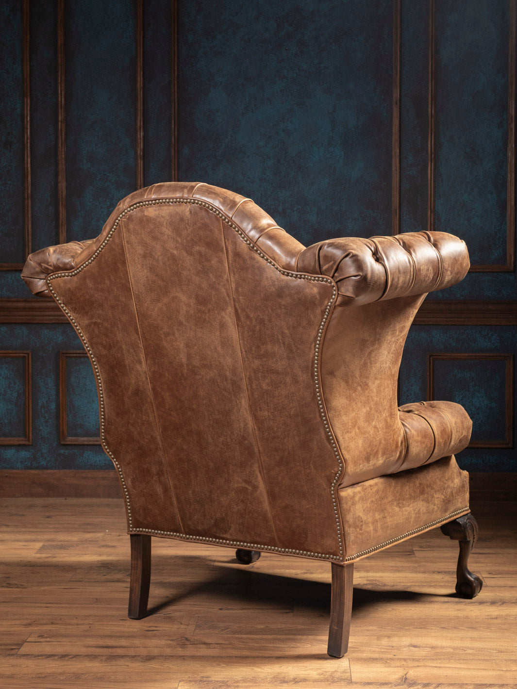 Back view of wingback chair in distressed leather with smooth curved frame and claw-foot base