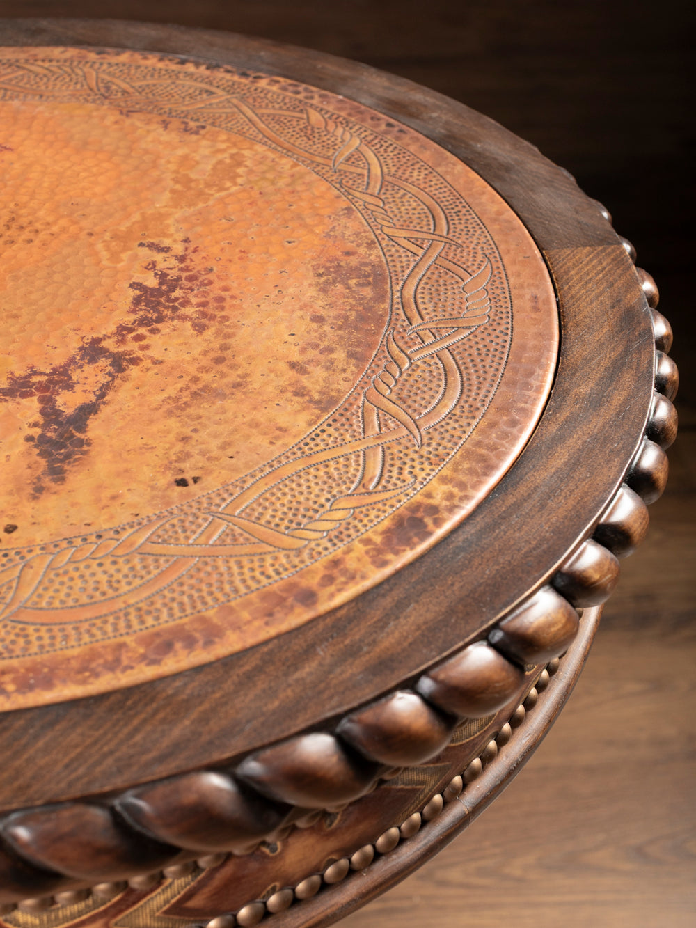 Close-up of hand-carved copper inlay tabletop with detailed hammered texture and carved wood edging on rustic western end table.