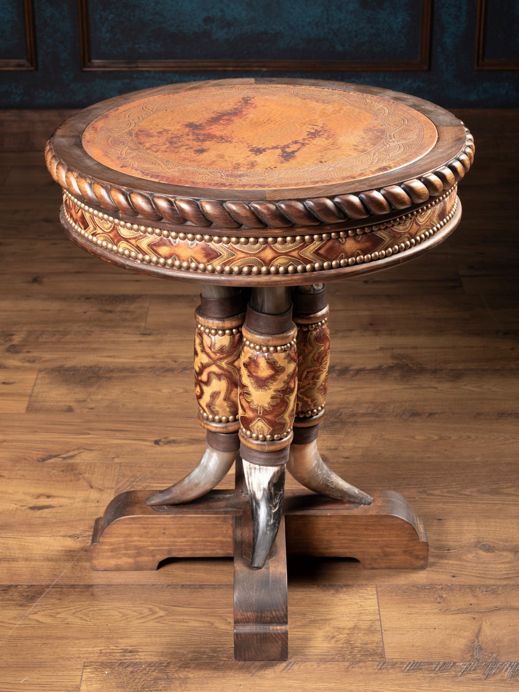 Angled view of rustic western end table showing copper inlay top, carved wood trim, and steer horn pedestal with embossed leather.