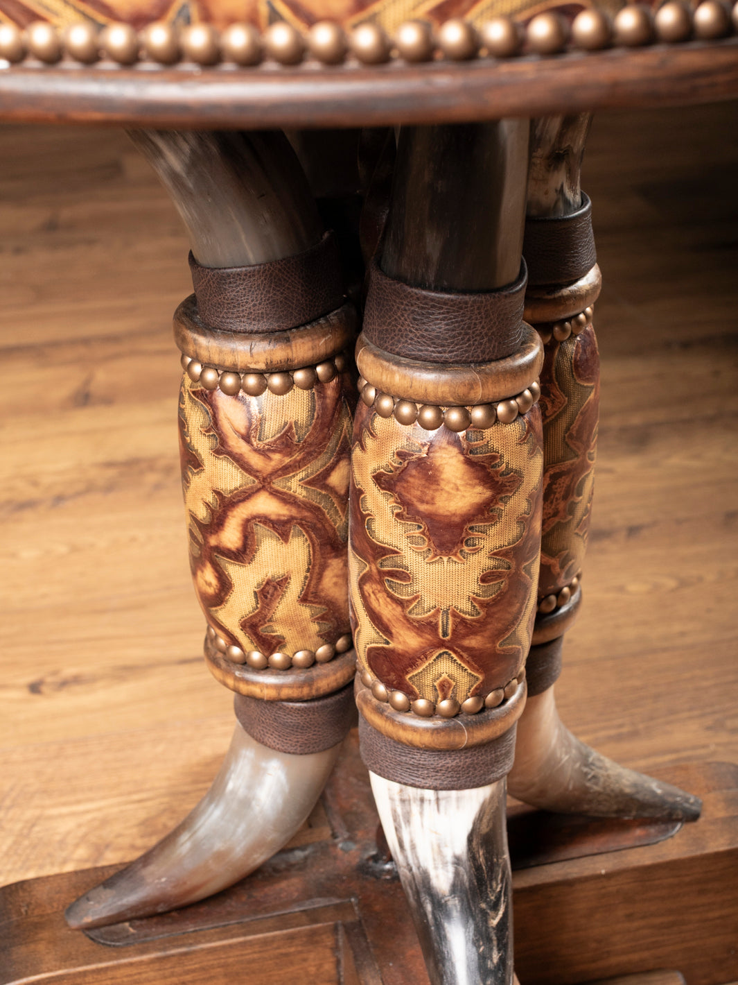 Steer horn pedestal legs wrapped in embossed leather and accented with nailhead trim on rustic western end table.