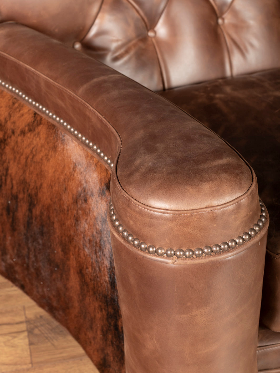 Arm detail view: Rolled leather armrest with nail trim and cowhide accent