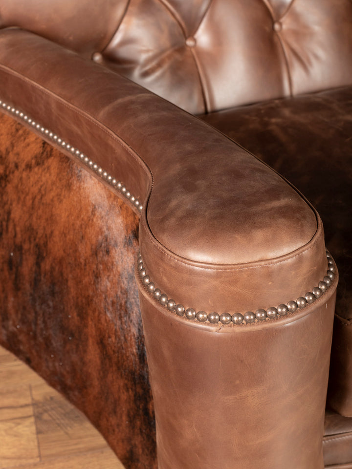 Arm detail view: Rolled leather armrest with nail trim and cowhide accent