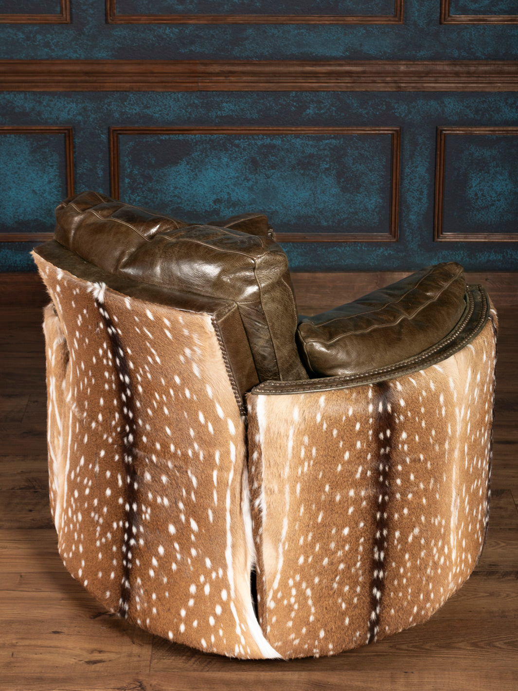 Chair with green leather and deer hide pattern against a wooden paneled wall.
