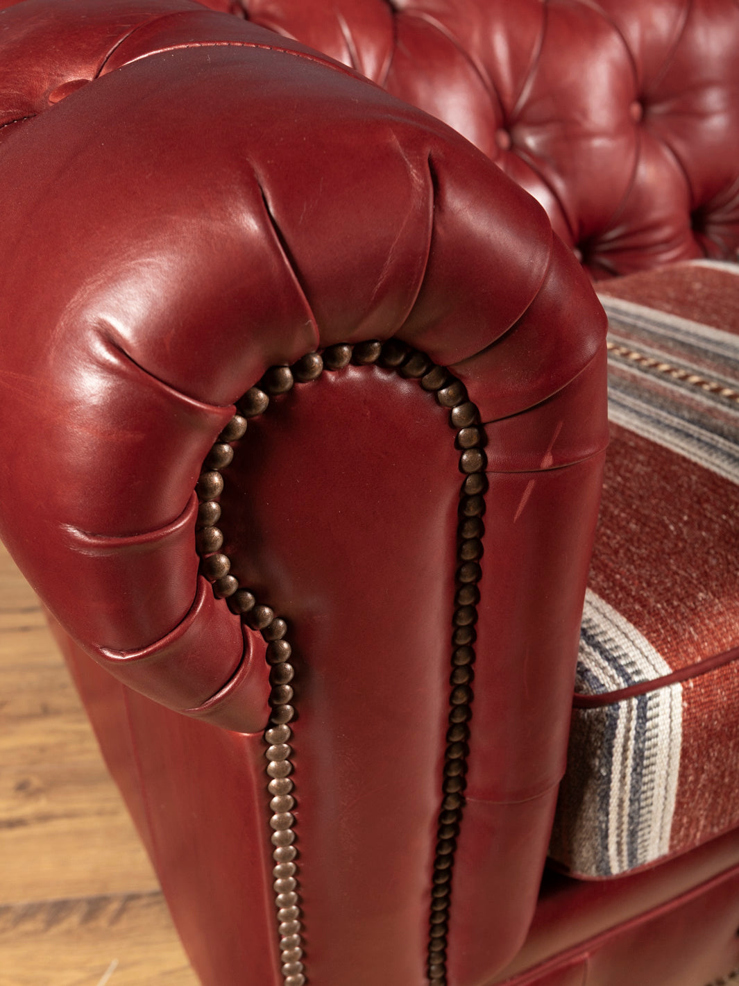 Extreme close up detail of pleated oxblood leather wrapping on a rolled Chesterfield sofa arm accented with individual antique brass nailheads.
