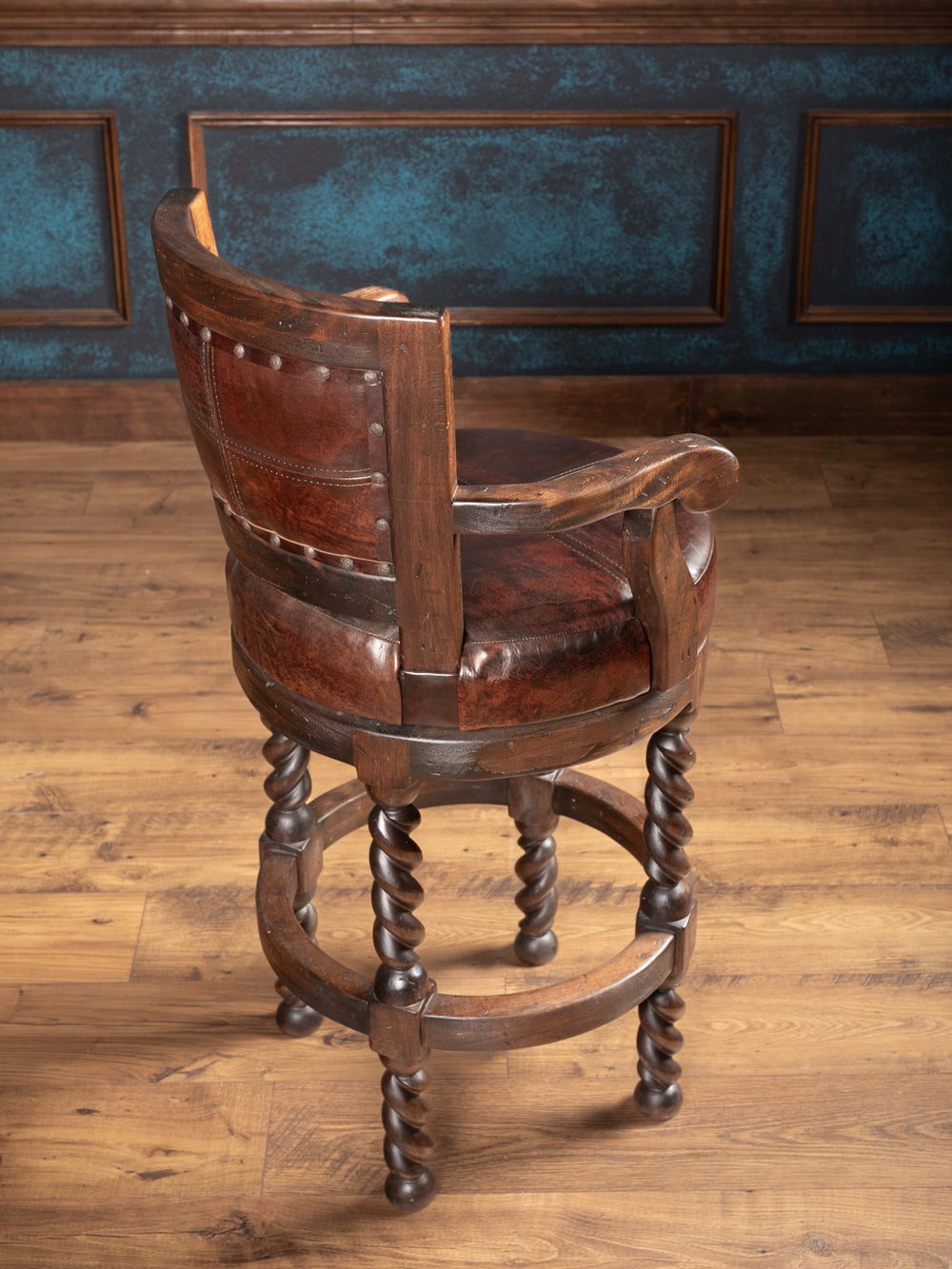 backside of vintage leather bar stool with twisted wooden legs on a floor against a blue wall.