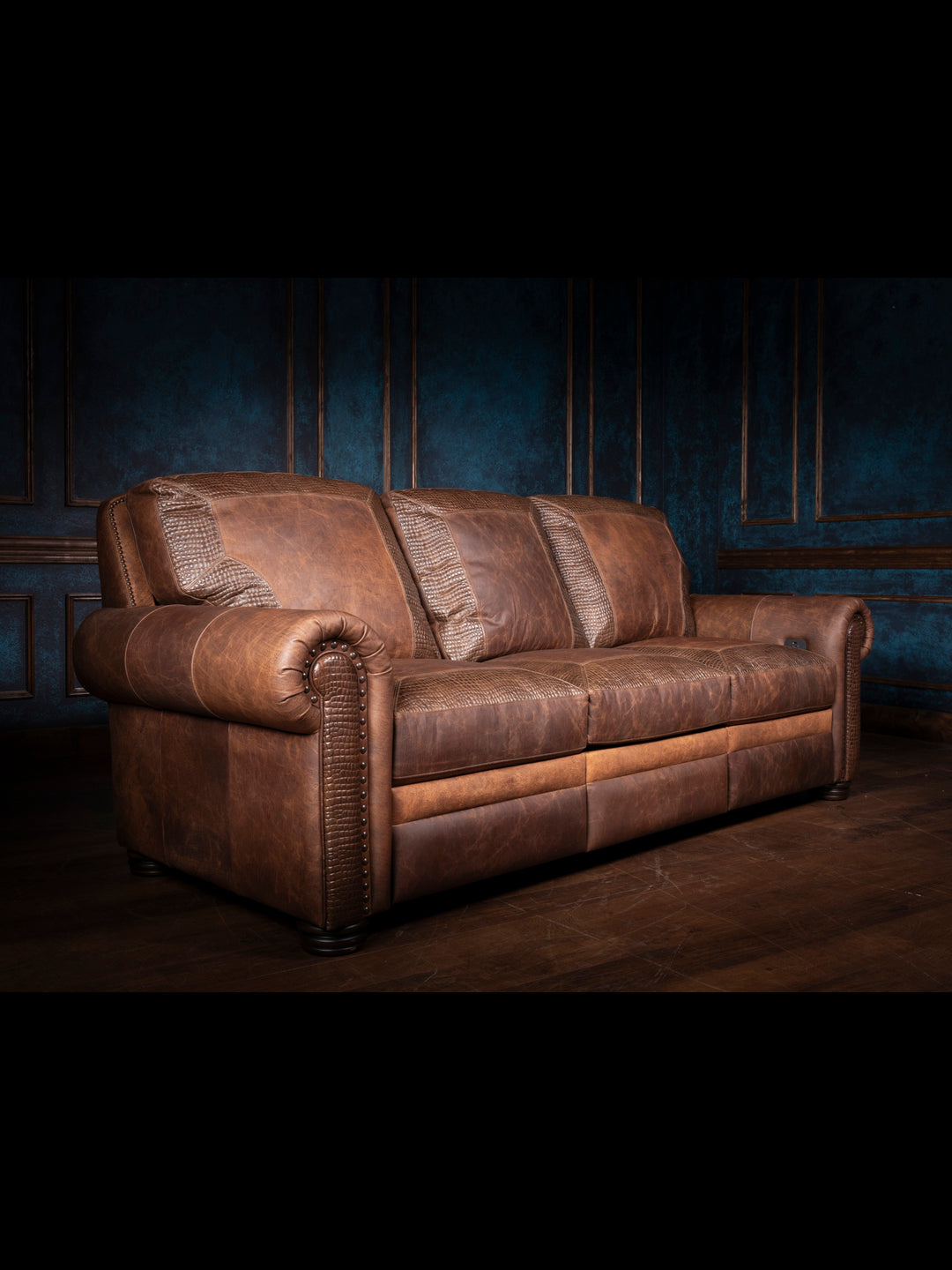 Bison Leather Power Recliner Sofa in distressed walnut leather with crocodile inlay, rolled arm design, and brass nailheads, shown in a rustic living room setting.