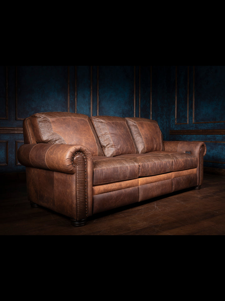 Bison Leather Power Recliner Sofa in distressed walnut leather with crocodile inlay, rolled arm design, and brass nailheads, shown in a rustic living room setting.