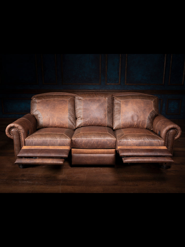 Three-seat Bison Leather Power Recliner Sofa upholstered in distressed Walnut leather with croc-stamped panels, rolled arms, and brass nailhead trim, shown with footrests extended in a rustic inspired room.