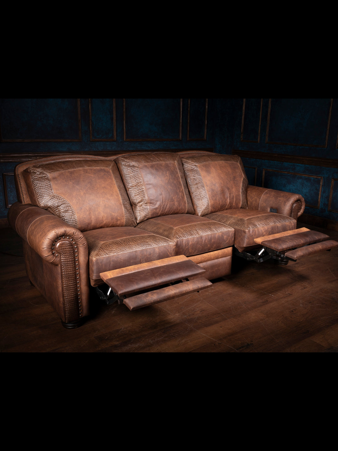 Bison Leather Power Recliner Sofa in distressed walnut leather with stamped croc accents and power reclining footrests, shown in a rustic interior setting