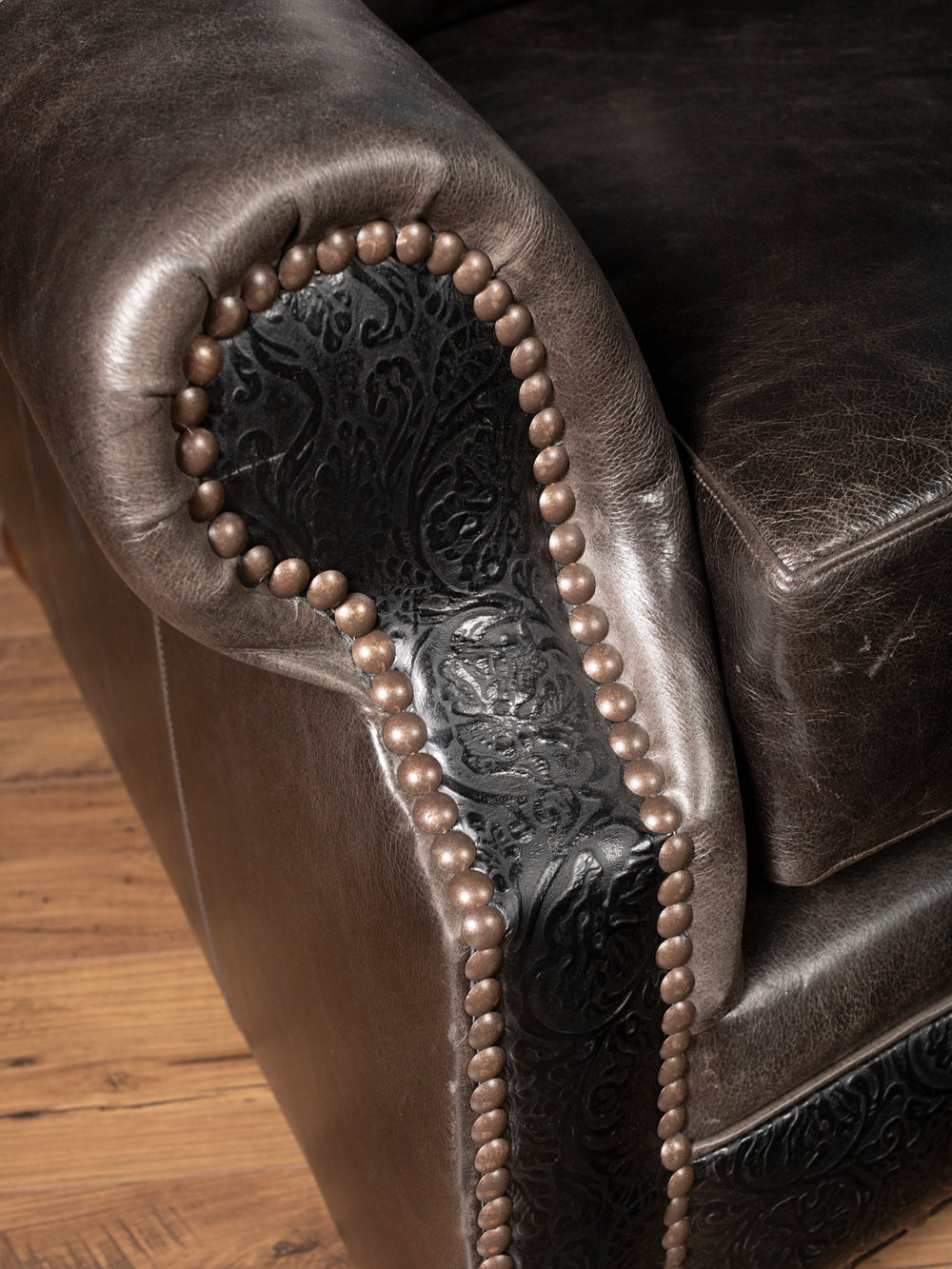 Close-up of hand-tooled floral leather detailing, nailhead trim, and full-grain buffalo leather on the rolled arm of the Brazos Western leather sofa.