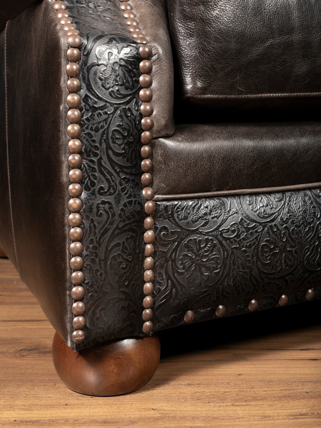 Close-up of tooled leather panels, decorative nailhead trim, and full-grain buffalo leather on the front rail of the Brazos handcrafted Western leather sofa.