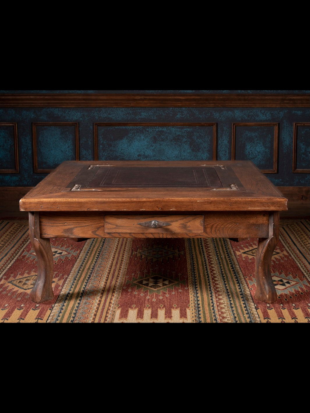 Nevada Cocktail Table with leather inlay top framed by brown wood featuring front storage drawer shown in a rustic living room.