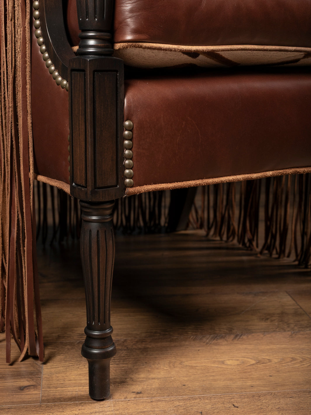Detailed close-up view of the dark-washed carved fluted wooden legs and premium raw-edge leather welting on a custom western armchair.