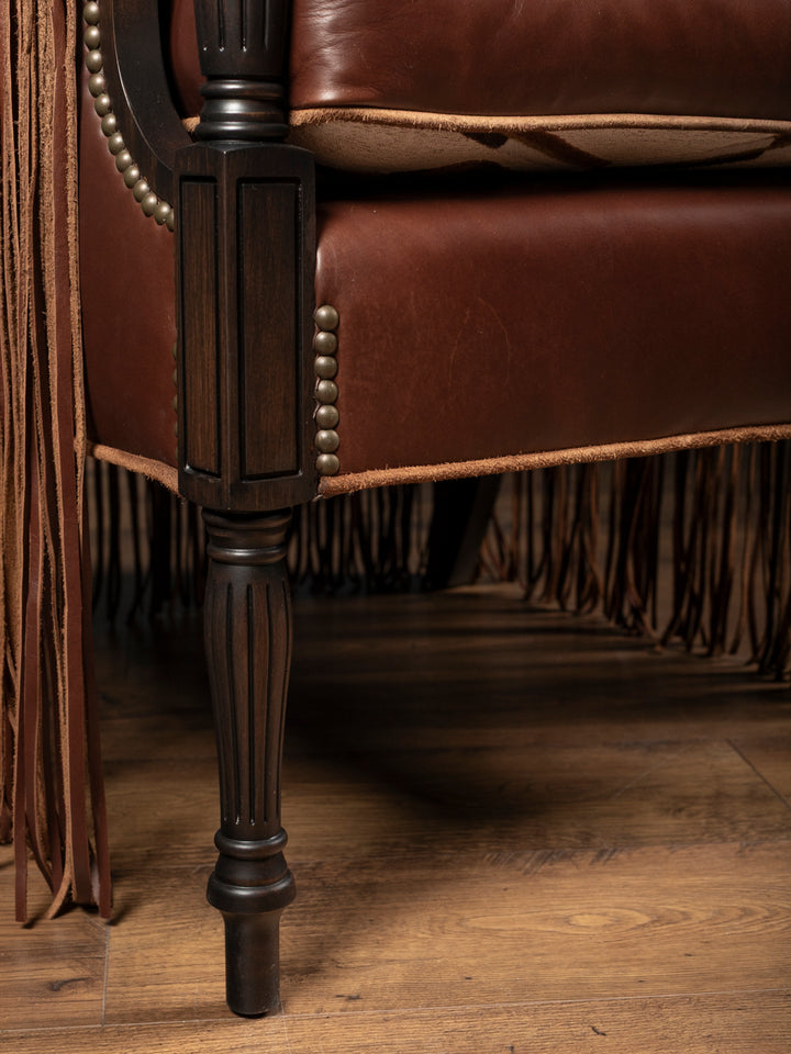 Detailed close-up view of the dark-washed carved fluted wooden legs and premium raw-edge leather welting on a custom western armchair.