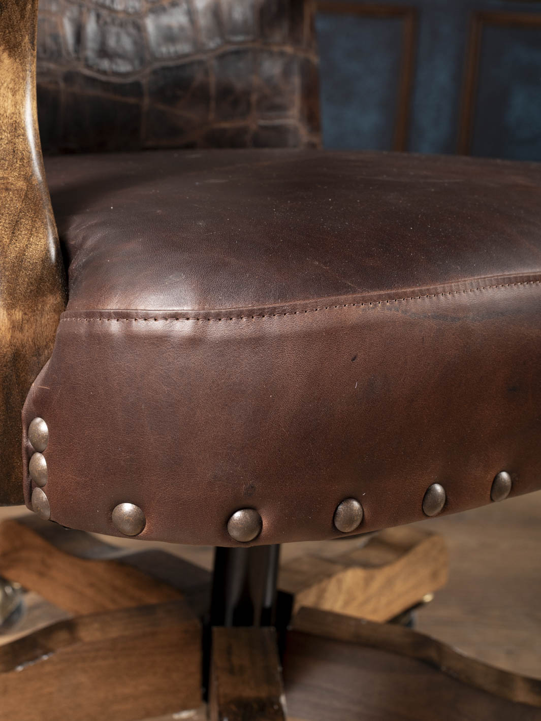 Close up view of the buttery soft chocolate aniline leather seat with heavy duty antique nailhead trim on a Western swivel office chair.