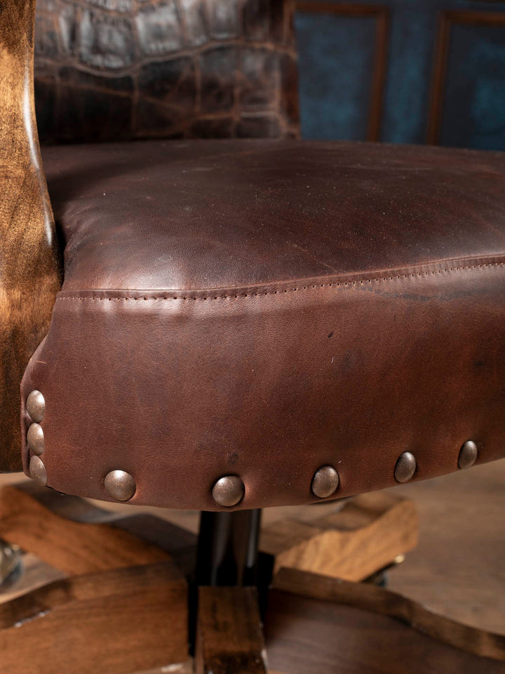 Close up view of the buttery soft chocolate aniline leather seat with heavy duty antique nailhead trim on a Western swivel office chair.