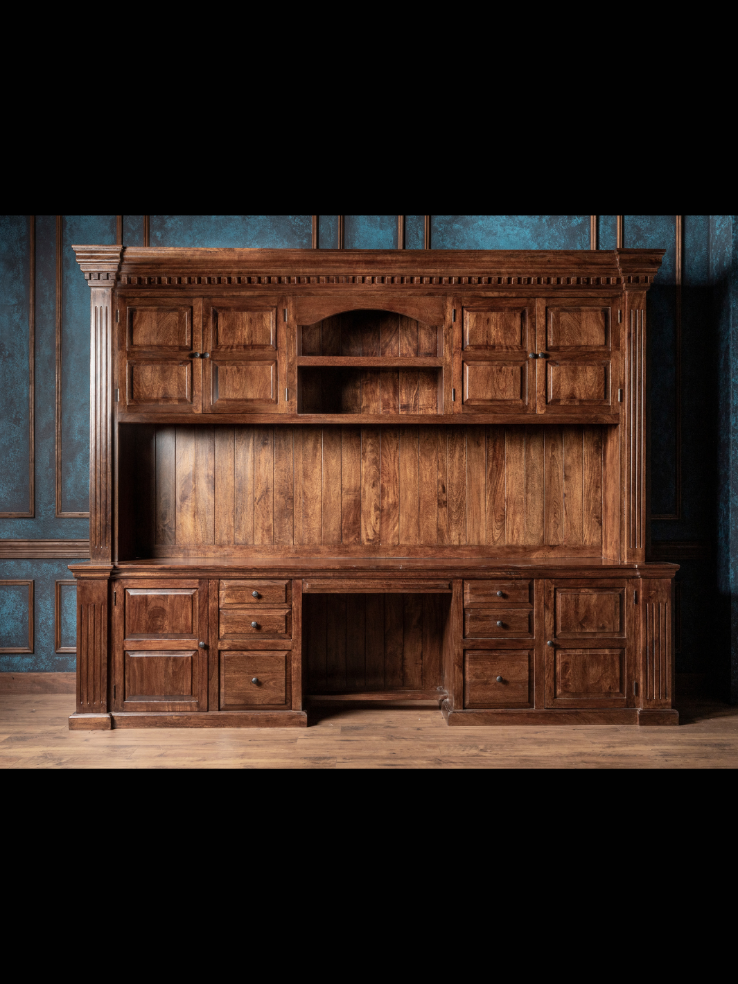 Large wooden desk with multiple cabinets and drawers against a blue wall.