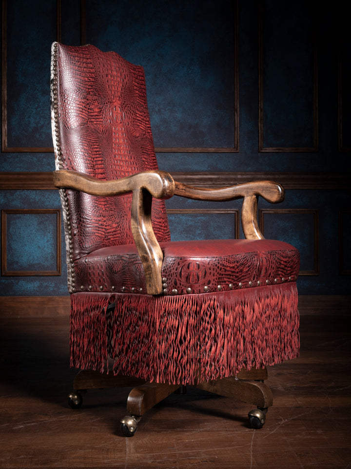 Crimson leather desk chair with fringe and wooden armrests in a luxury office setting, showcasing rich textures and unique western design.