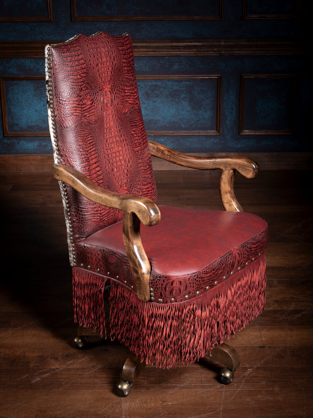 Full view of a crimson embossed leather desk chair with fringe and antique-style wooden legs in an elegant office.