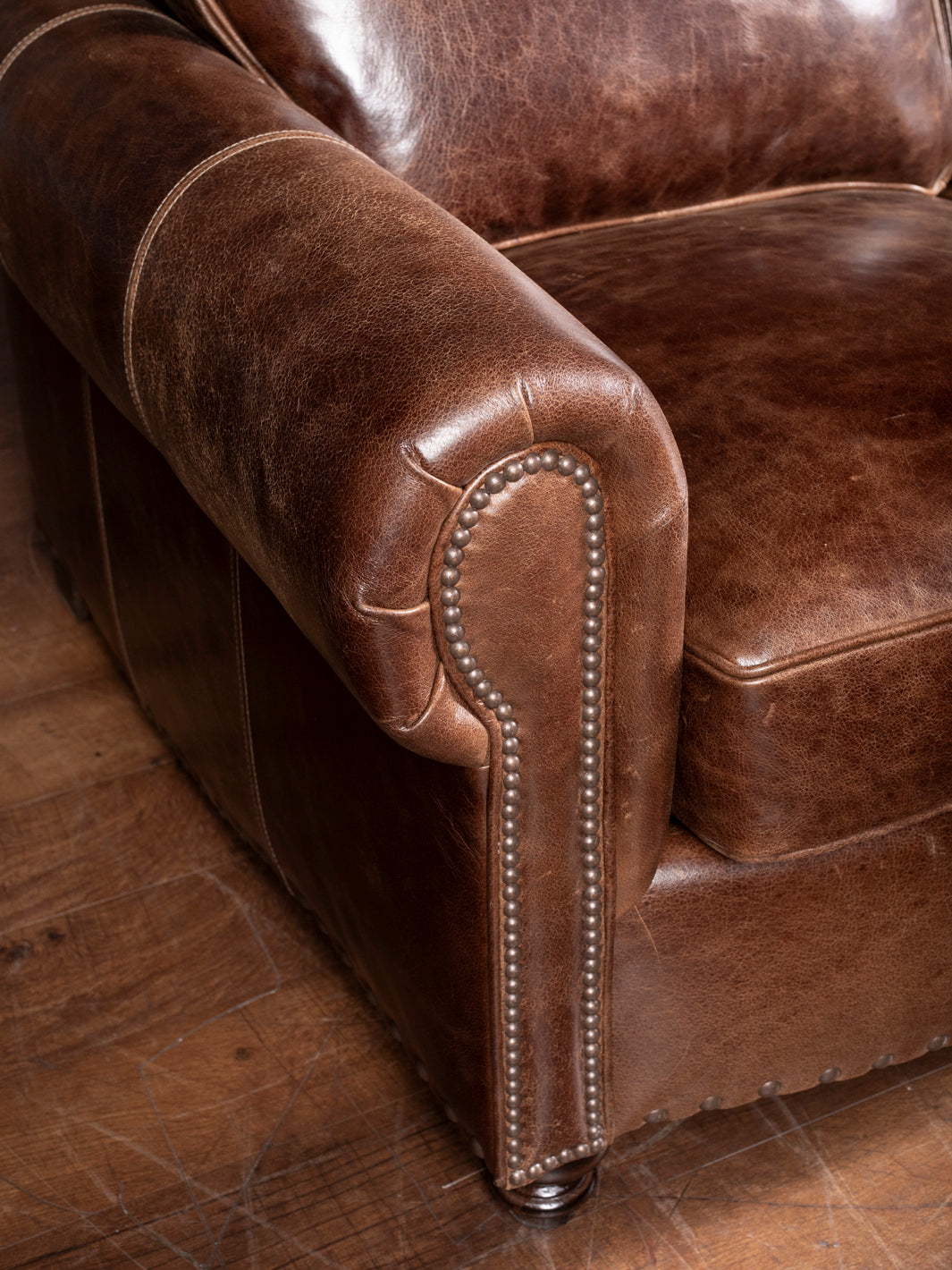 Dark Rum Rolled Arm Sofa in brown full-grain buffalo leather with brass nailheads on arm trim in a close-up view.
