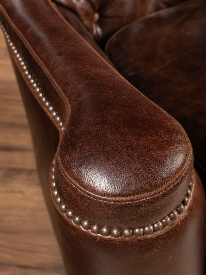 Nailhead trim detail along the curve of the Dark Rum tufted leather swivel chair