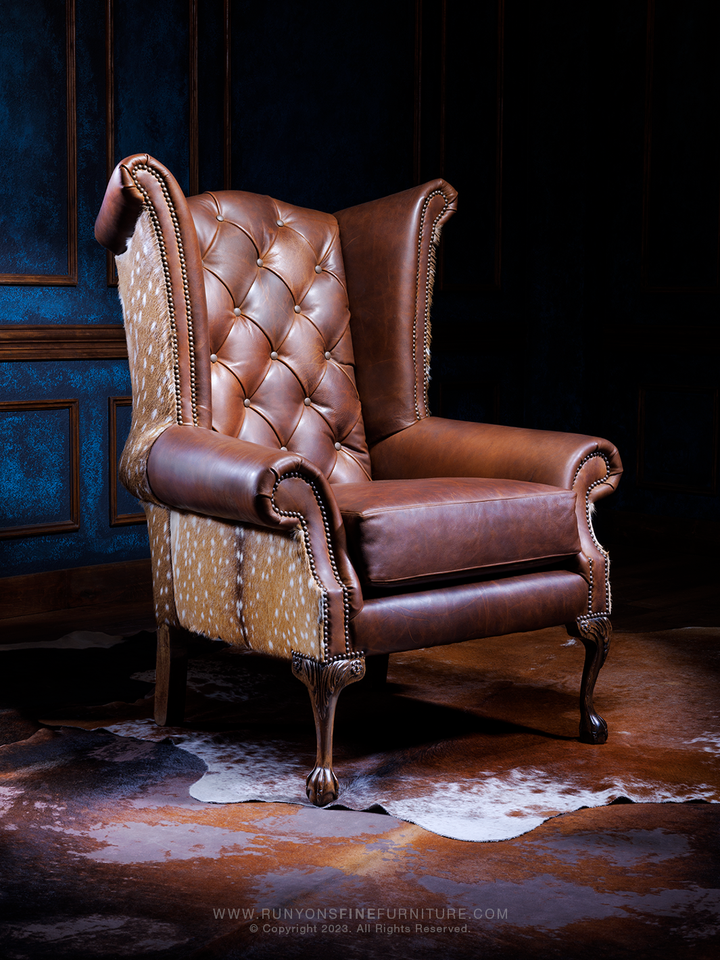 Elegant Axis Leather Accent Chair in Red Oak full-grain leather with tufted inside back, wingback sides, Axis hair-on-hide accents, and carved wood legs, shown in a western living room setting.