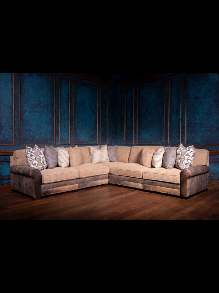 Sectional sofa with patterned pillows against a dark blue wall.